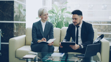 Two female and male business colleagues with clipboard and notepad having conversation at hotel...