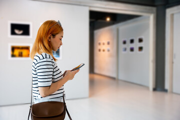 Visitor woman standing takes picture art gallery collection in front framed paintings pictures with...
