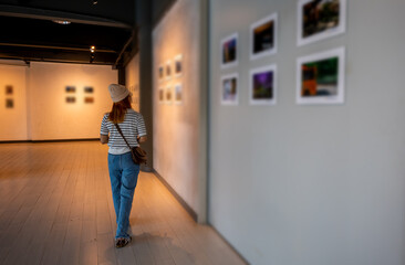 Asian woman walking through art gallery collection in front framed paintings pictures on white...
