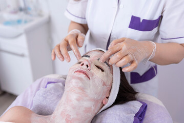 Obraz na płótnie Canvas Cosmetologist applying a face mask to a client's face in a beauty salon, spa