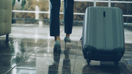 legs of businesswoman walking through hotel lobby pulling luggage and stop at reception desk...