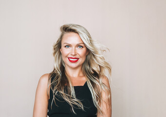 Portrait of gorgeous beautiful blonde young woman with bright makeup in evening dress on beige background