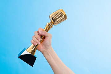 Hand holding golden microphone trophy on blue background