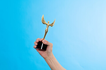 Hand holding golden statuette trophy on blue background