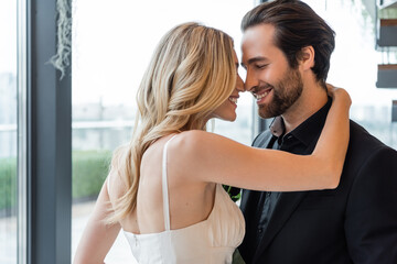Side view of smiling blonde woman embracing boyfriend in suit in restaurant.