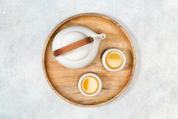 A white teapot and two cups of lemongrass tea on a wooden tray. View from above.