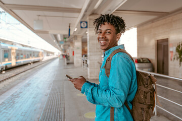Fototapeta premium Smiling guy standing sideways to camera near railroad
