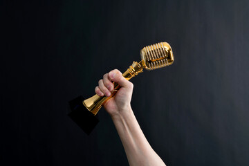 Hand holding golden microphone trophy on black background