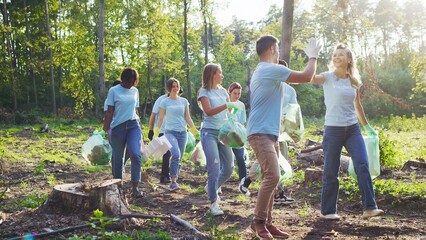 Group of eco activists in same t shirts collecting garbage and carrying bin bags. Concept of cleanup, care about nature and ecology