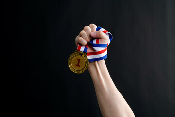 Human hand holding gold medal on black background