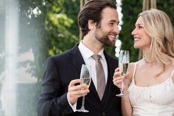 Cheerful newlyweds holding glasses of champagne outdoors.