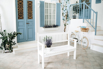 White bench with live lavender in a pot in the patio of a white mediterranean house with a blue door and window, a flowering tree and a vintage bicycle against the wall. House in Santorini