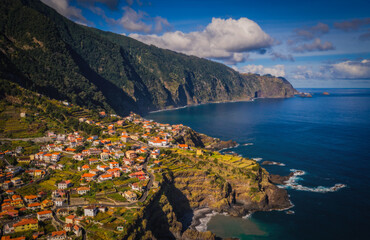 Fototapeta premium Amazing aerial view of red roofed houses located amidst green fields near Seixal beaches washing by ocean in Madeira, Portugal. October 2021