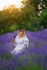 Fototapeta na wymiar Romantic young woman in a white dress and straw hat in a lavender field on the sunset 