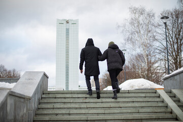 Guy and girl walk through city. Man leads girl under his arm.