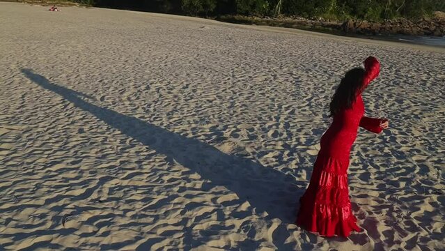 Woman in red dress training flamenco spin on beach sand at sunset. Gimbal