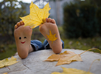 yellow autumn leaf between the toes on the bare feet of a toddler child. painted smile on the feet....