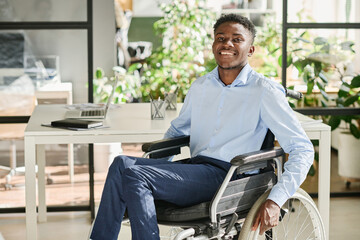 Portrait of African businessman with disability sitting in wheelchair and smiling at camera during...