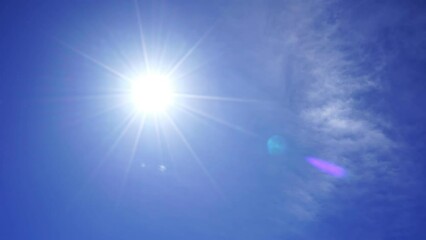Nature view of direct bright noon sun on blue sky with clouds Sun shining on summer horizon in vibrant sunlight Sunbeam and sun ray flares with white cumulus clouds in midday sunshine day
