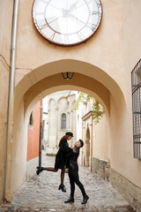 Fototapeta na wymiar Sweet couple in the yard of the old town. The guy lifts the girl up, November 2, 2019, Lviv, Ukraine.