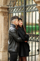 Stylish couple posing near a wrought iron gate in the yard.