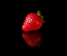 Single ripe red strawberry on a black reflective background