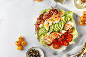 Cobb salad with grilled chicken, eggs, avocado, tomato, bacon on marble white background. Keto diet.