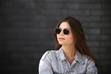 Close up portrait of a fashionable young woman in modern sunglasses over brick wall background. Street style. Beauty, fashion concept. Optics, eyewear.