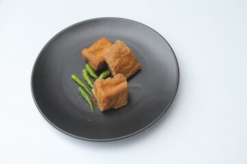 Square fried tofu with green chili on black round plate on white background