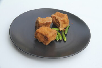 Square fried tofu with green chili on black round plate on white background