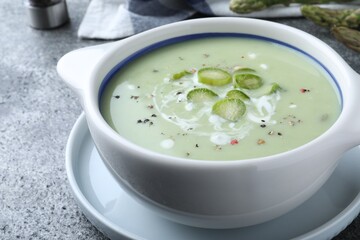 Bowl of delicious asparagus soup on grey table, closeup