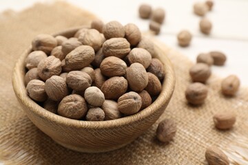 Scattered nutmeg seeds, bowl and sack cloth on white table, closeup
