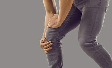 Close up crop of man on grey studio background have kneecap spasm. Acute pain in knee area....