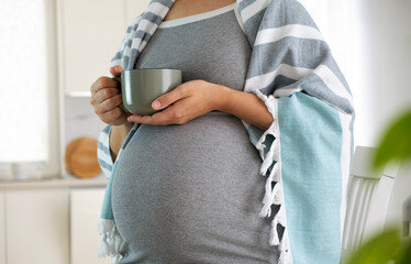Pregnant woman wrapped in blanket with cup in hands drink hot tea. Natural treatment, remedies, homeopathy to treat illness while pregnancy. Herbal tea for healthy pregnance.