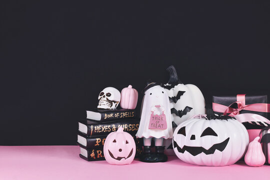 Pink and white Halloween decor with black and white pumpkins, spell books and spiders on black background  with copy space