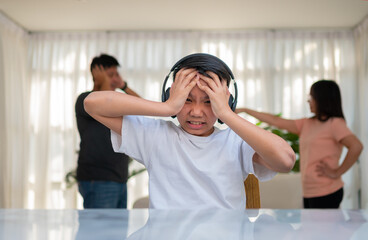 Asian boy kid wearing headphones and play loud music. so as not to hear quarrel while parents having fight or quarrel conflict at home. Unhappy problem in family, Domestic problems in the family.