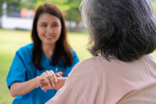 Asian careful caregiver or nurse hold the patient hand and encourage the patient in a wheelchair.  Concept of happy retirement with care from a caregiver and Savings and senior health insurance.