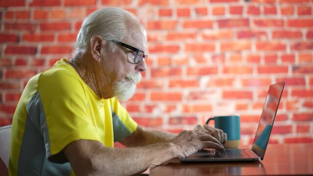 Side view profile of unhappy elderly old man sitting at desk using laptop computer tired and getting bad news.