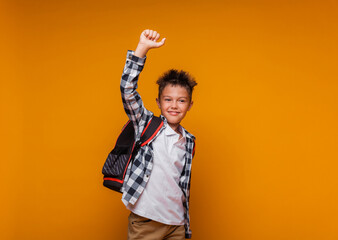 A student greets on a yellow background. portrait of a boy with a backpack and a folder.