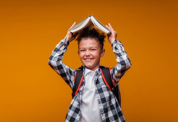 Portrait of a schoolboy boy holding a book over his head, with a bag, backpack, isolated on a...