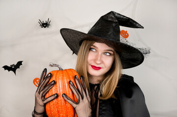 Halloween portrait of beautiful blonde with pumpkin against background with spiderweb with bats and spiders on it.