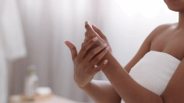 After shower body care. Unrecognizable african american woman wrapped in towel rubbing pampering lotion on hand