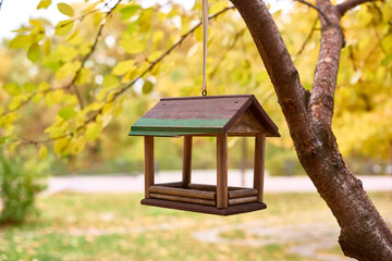 brown bird feeder hanging on tree branch with yellow leaves, fall landscape. selective focus, background blur