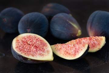 red sliced ​​fresh figs lie next to each other against a dark background. Many figs are also closed behind.