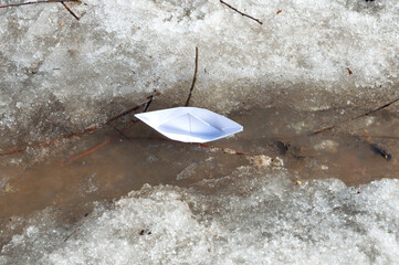 Top view of white paper boat sails along a spring stream among the snowy shores