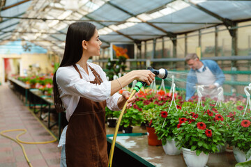 White woman and man wearing aprons working with plants in greenhouse