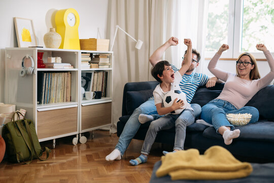 Family Of Three Cheering And Watching Soccer Game At Home