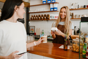White brunette woman using cellphone while buying coffee in cafe