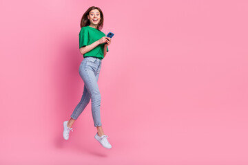 Full length portrait of excited energetic person jump hold telephone empty space isolated on pink color background