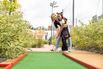 little girl and mother playing mini golf - obrazy, fototapety, plakaty